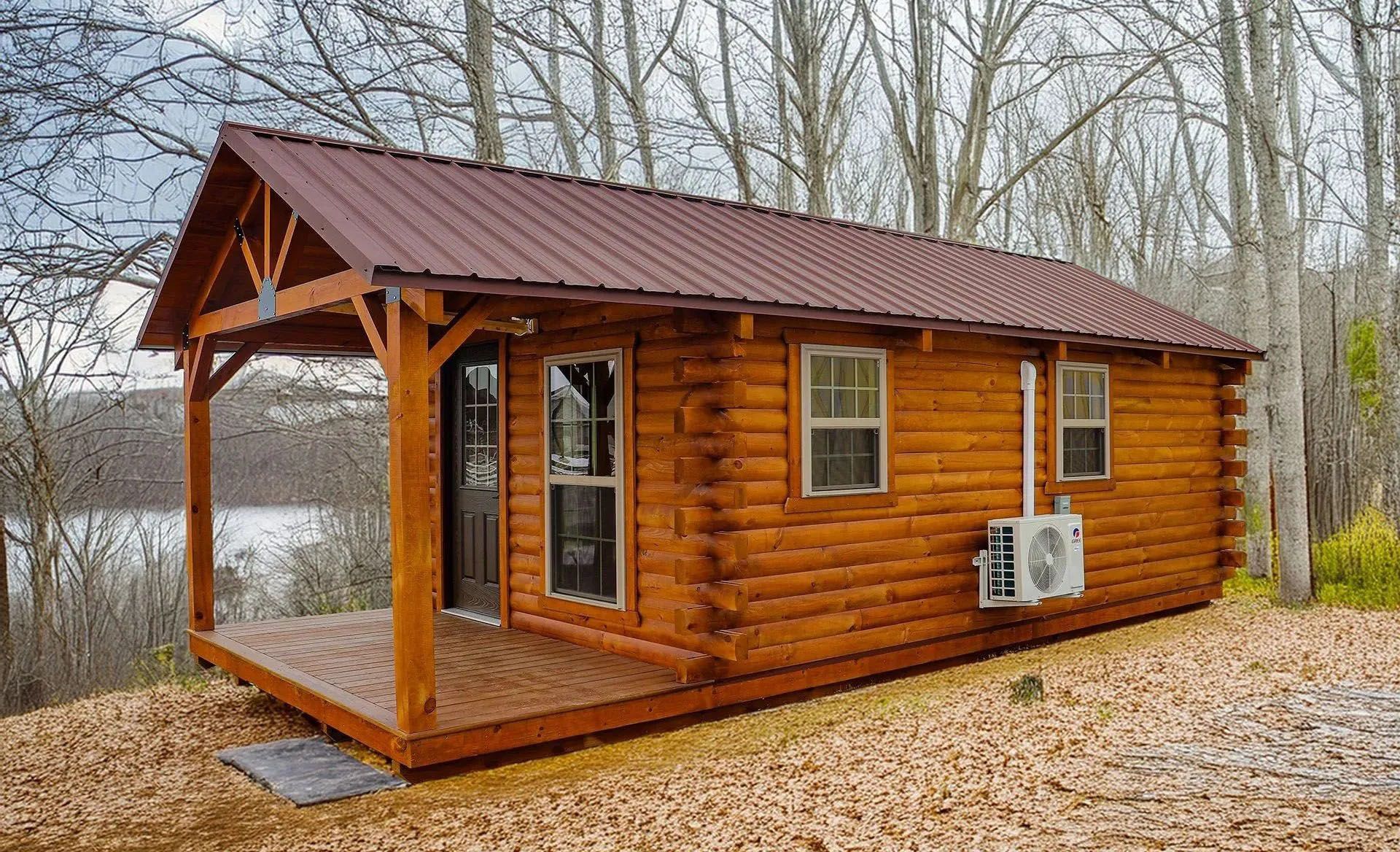 Wooden cabin with porch and brown metal roof sits in a wooded area near water.