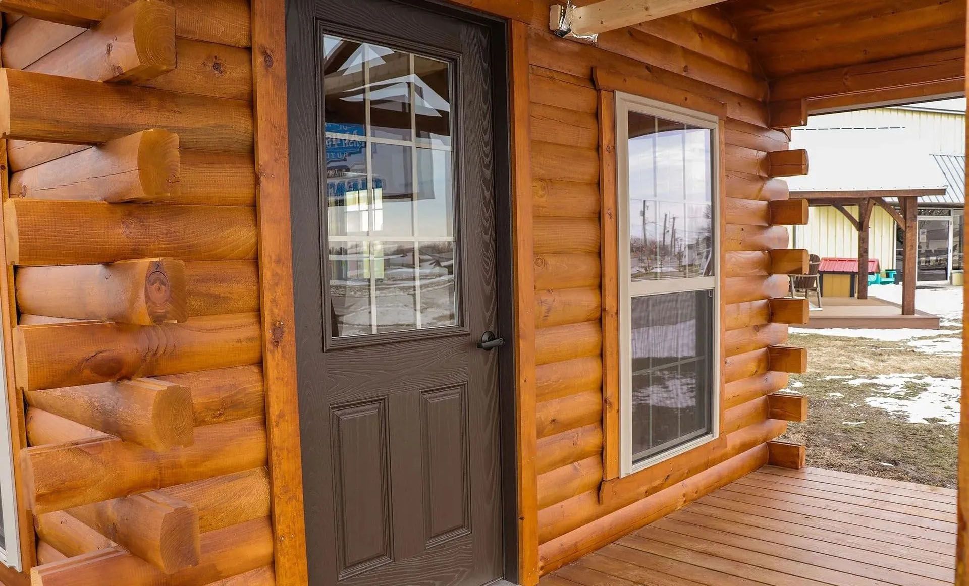 Log cabin exterior with brown door, window, and porch, logs stained orange-brown.