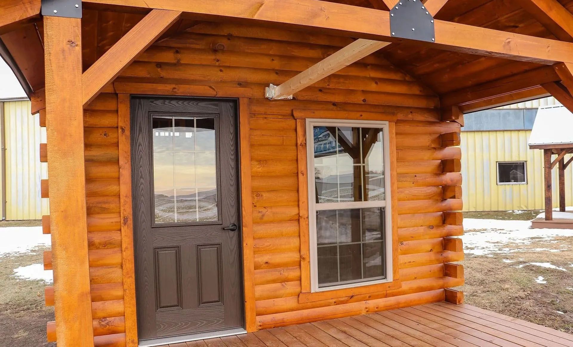 Log cabin with brown door and window, under a wooden overhang.
