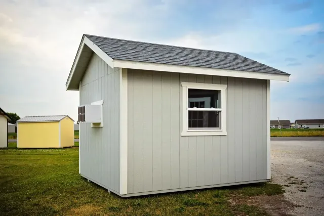 Gray shed with white trim, window, and dark gray roof, set on grass.