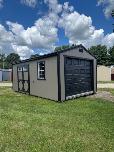 A tan storage shed with black trim, a garage door, a side door with windows, and a single window, set on a grassy lot.