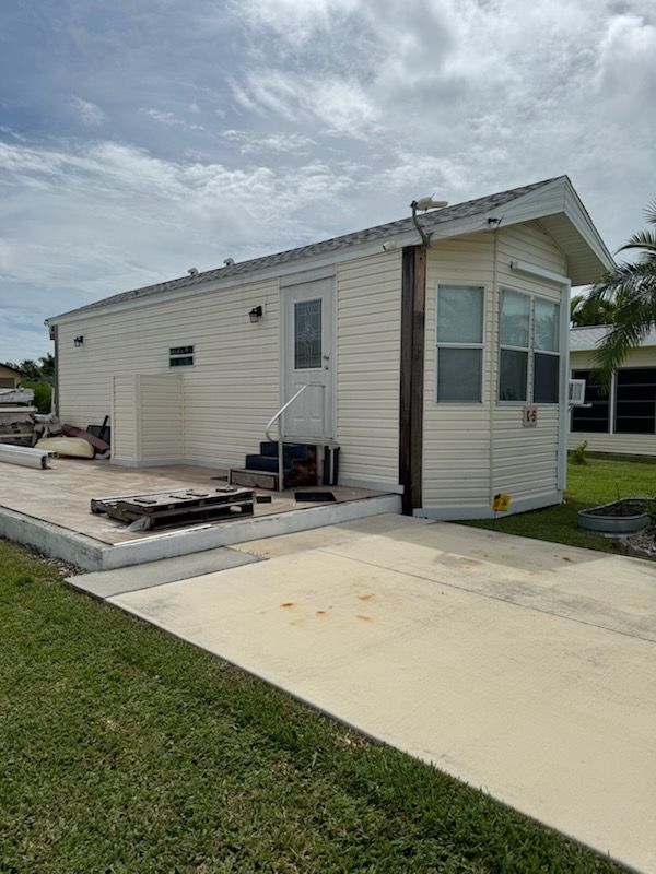 Light yellow mobile home with a small porch and driveway. Blue sky overhead.