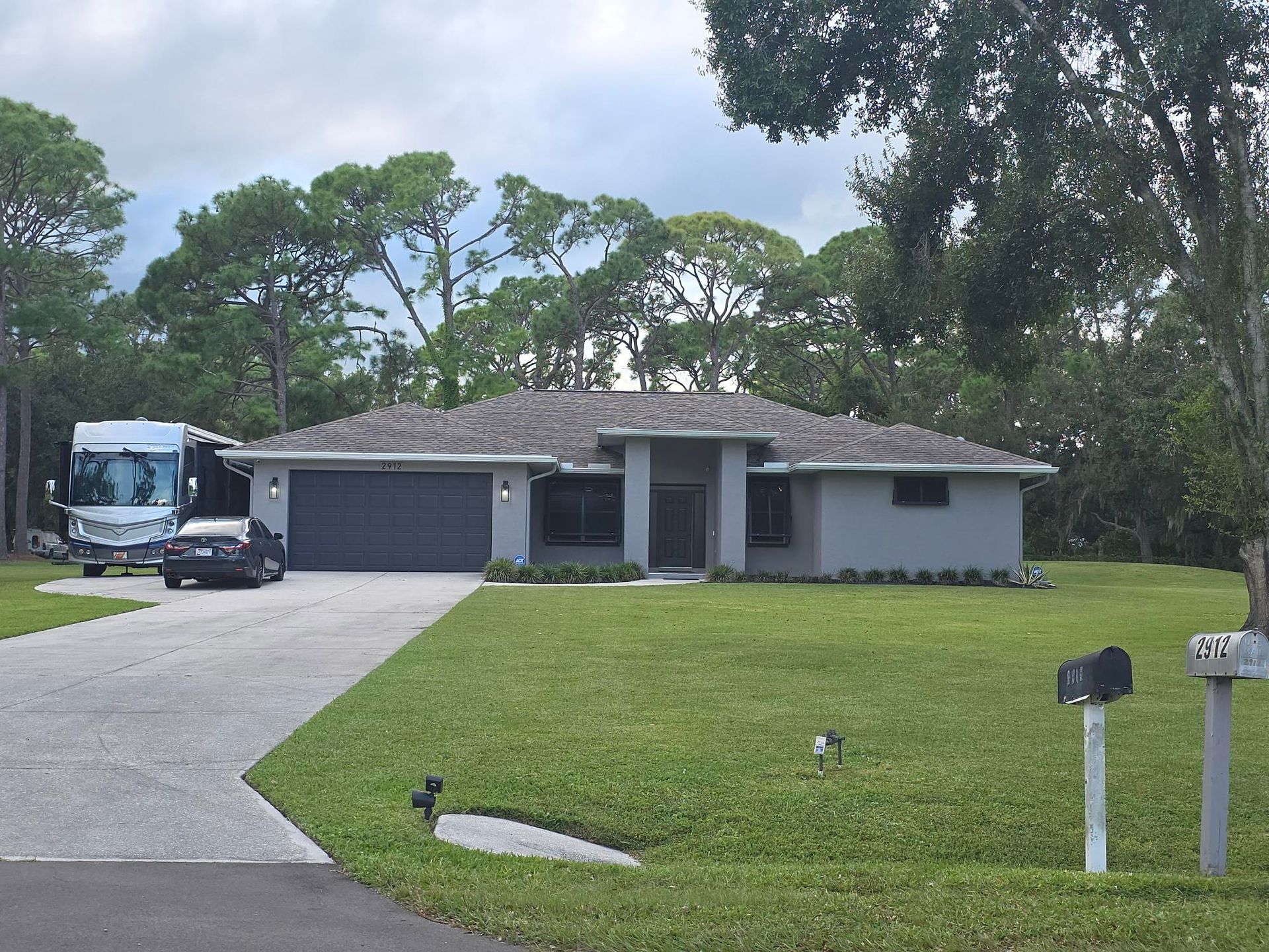 Gray house with a gray garage door, green lawn, driveway, and a recreational vehicle.