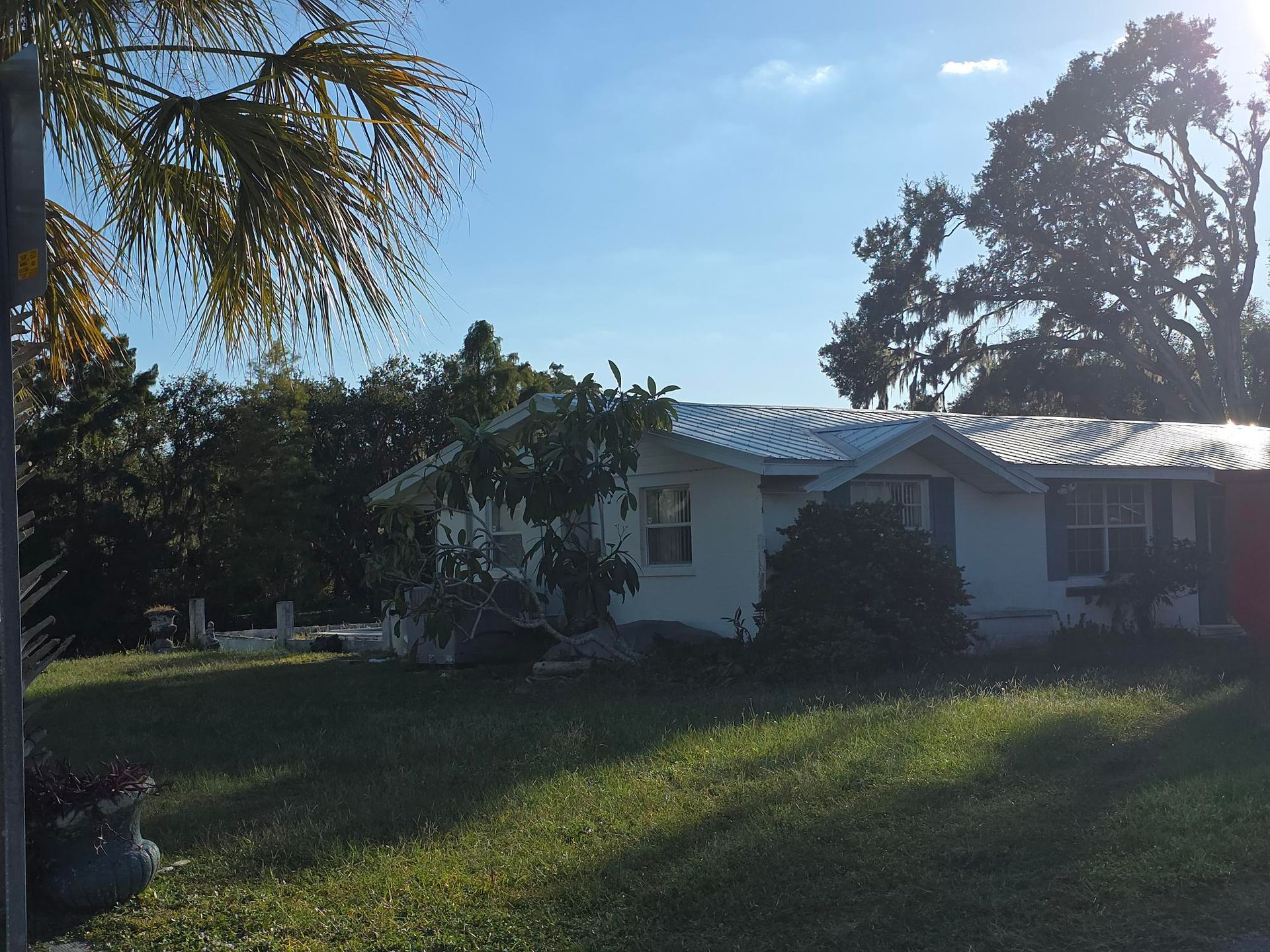 White house with a silver roof, trees, and green grass on a sunny day.
