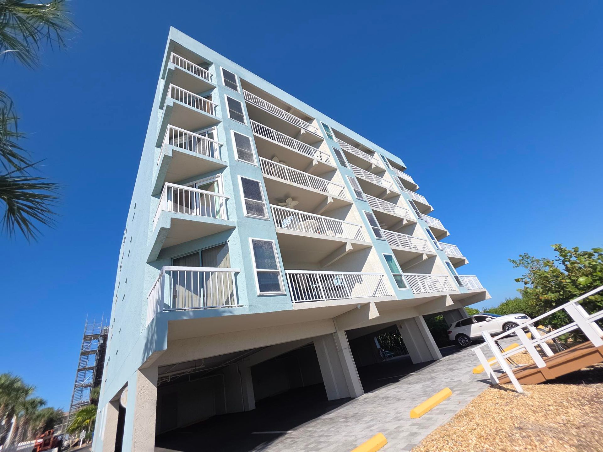 Blue multi-story building with balconies, bright blue sky in background.