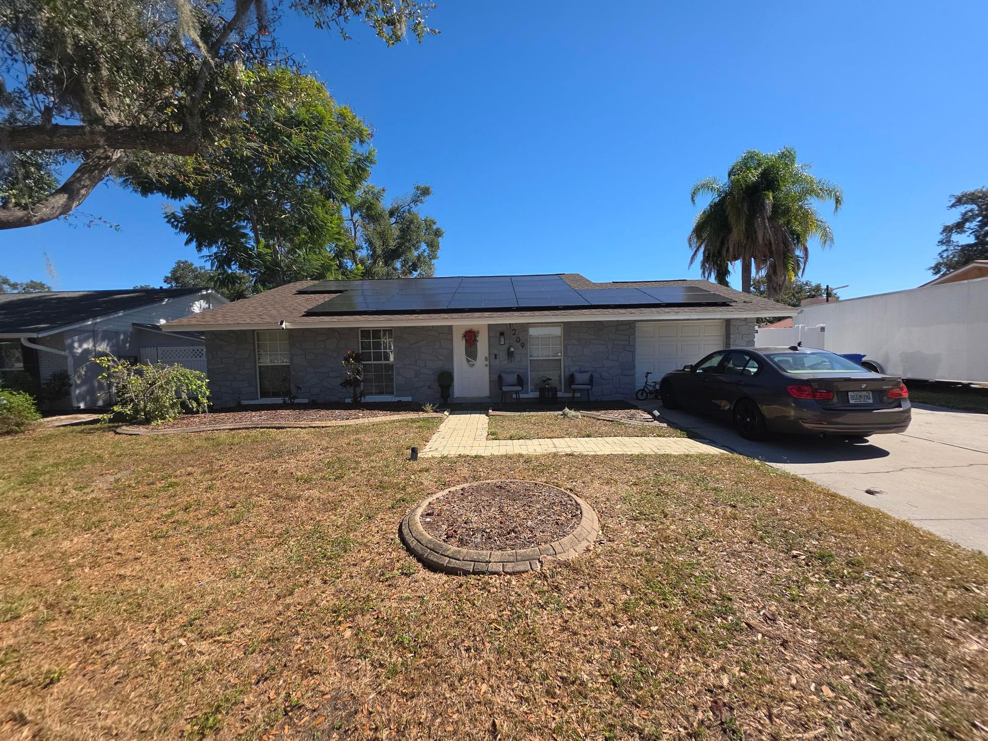 A house with solar panels on the roof and a car parked in the driveway on a sunny day.
