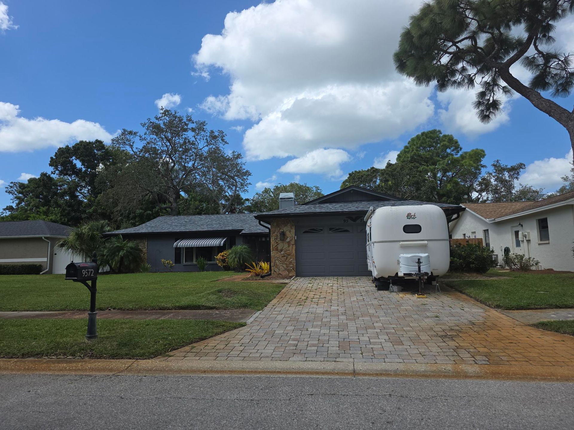 A single-story house with a trailer parked in the driveway on a sunny day.