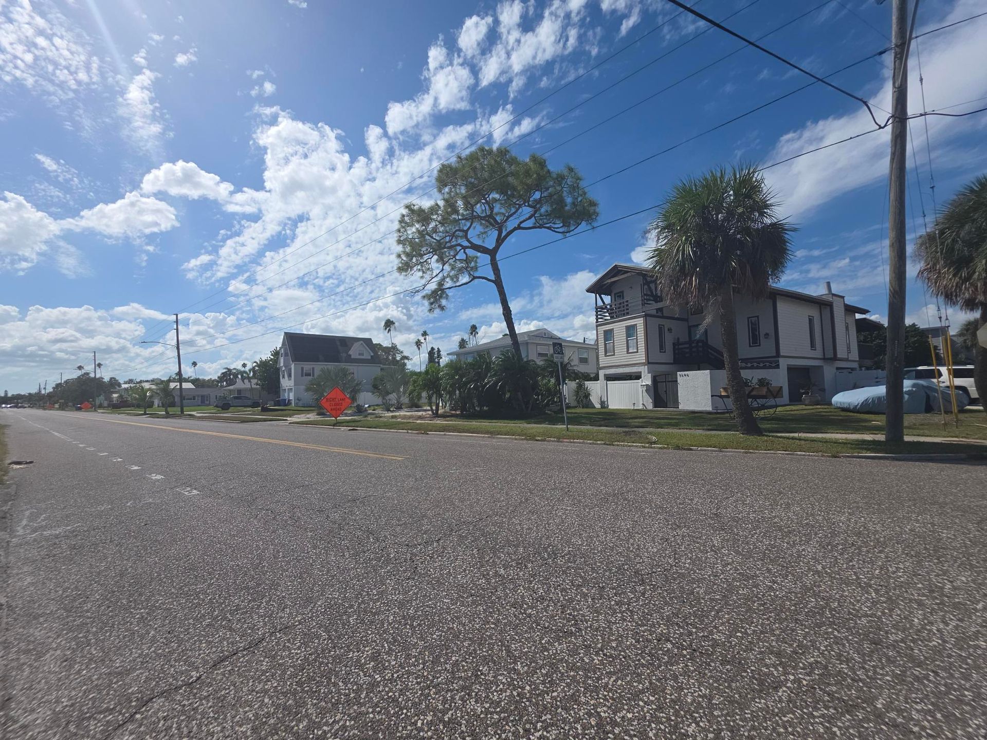 Street view of houses on a sunny day. Paved road, blue sky with clouds.