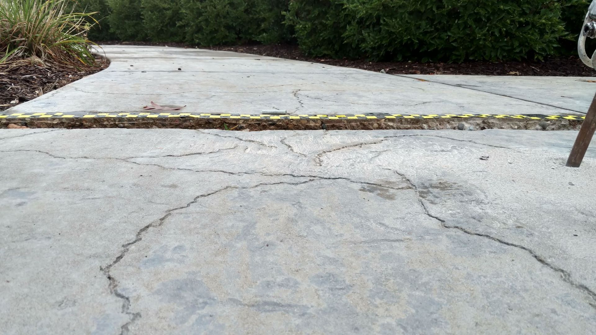 A cracked concrete walkway with a yellow stripe on the side - before