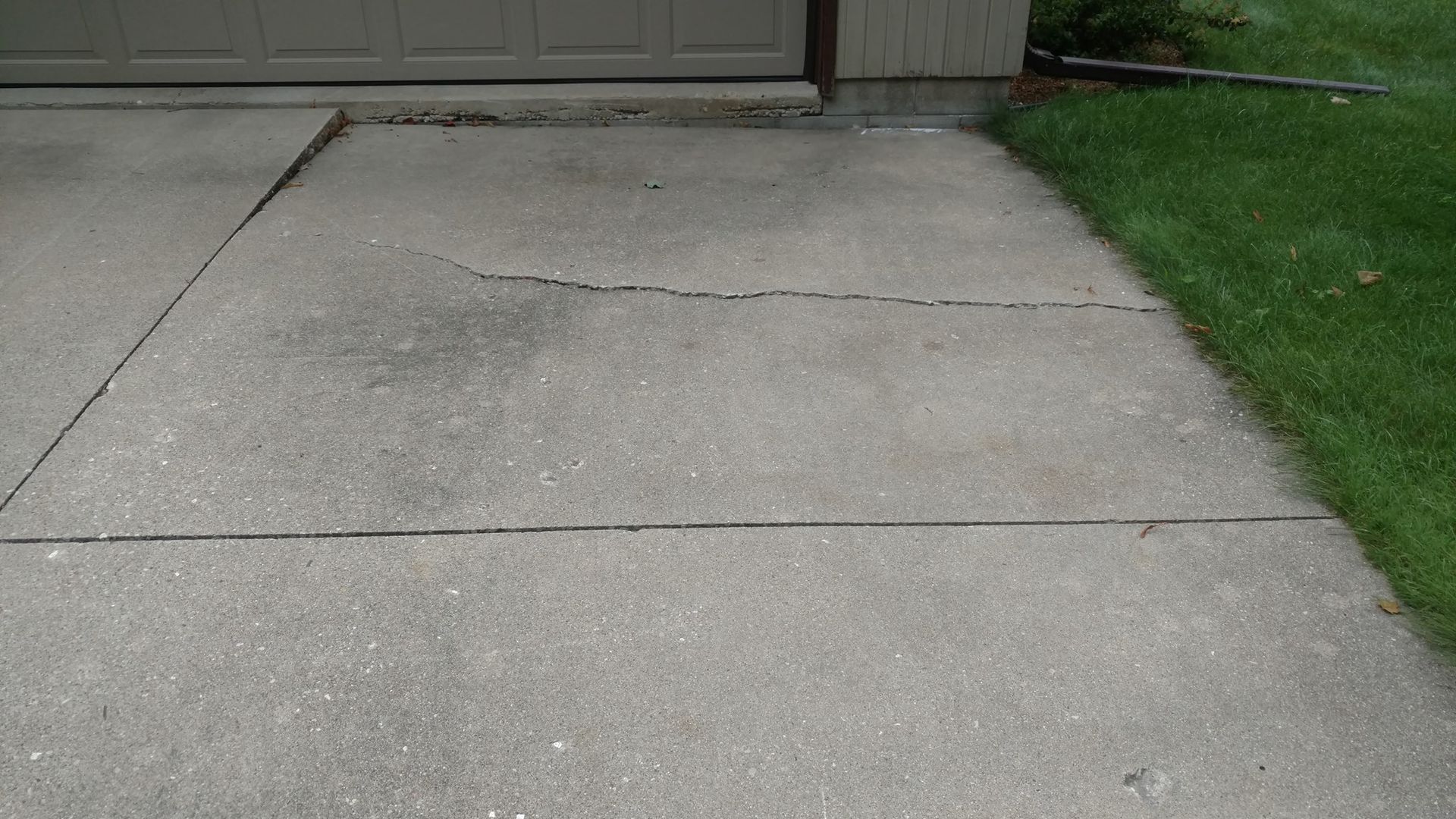 A concrete driveway with a garage door in the background - before