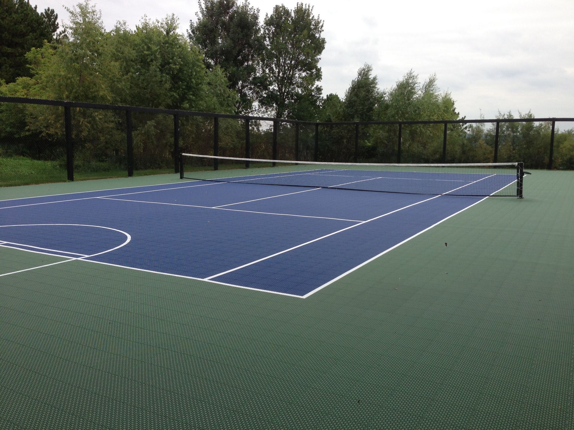 A blue and green tennis court with trees in the background