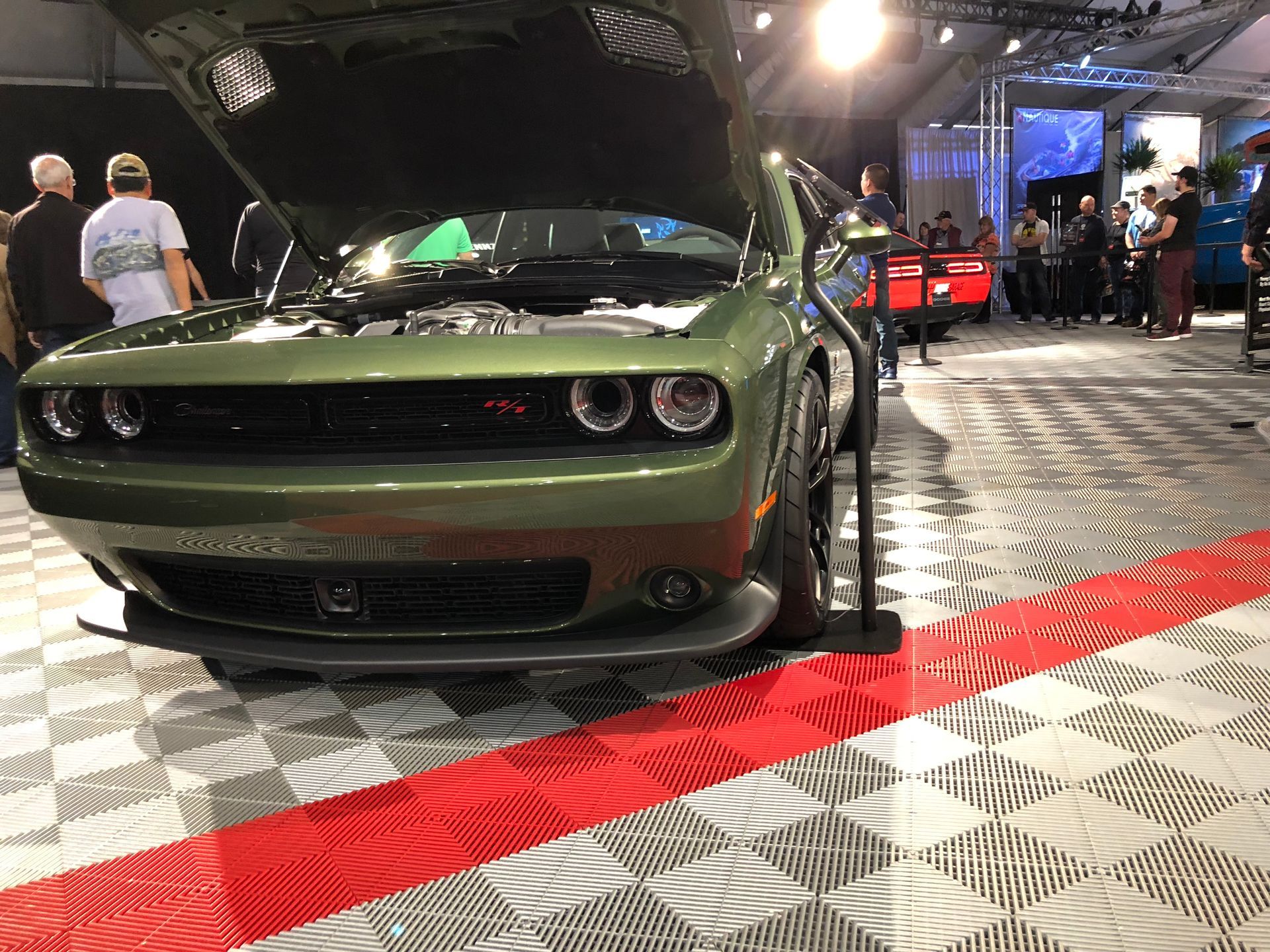A green dodge challenger with the hood up is on display at a car show.