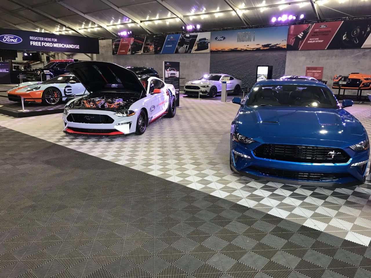 A blue mustang is parked next to a white mustang at a car show.