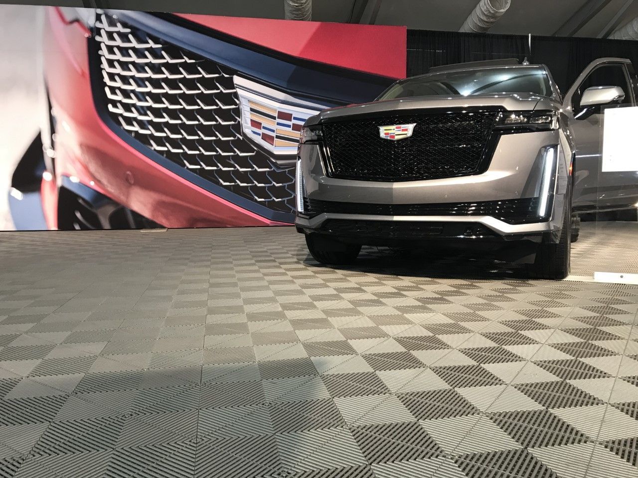 A cadillac is parked in a showroom with a checkered floor.