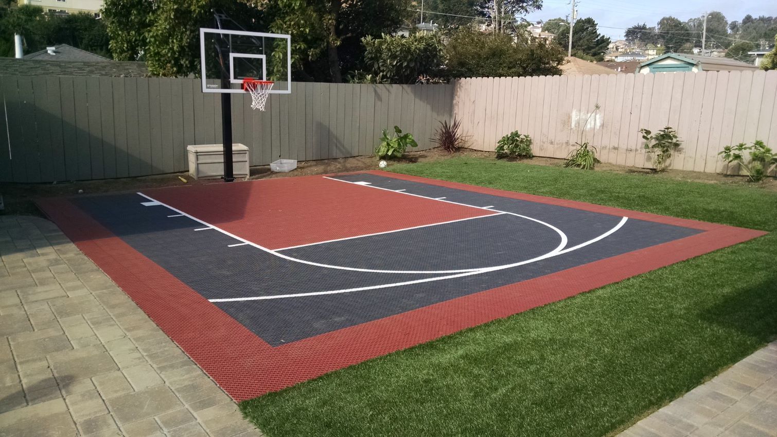 A basketball court in a backyard with a fence in the background