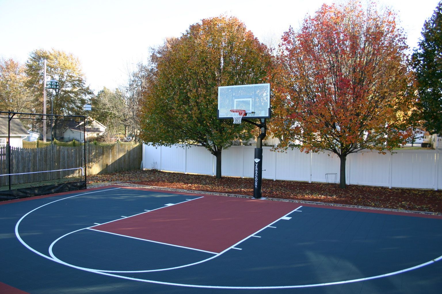 A basketball court with a white fence and trees in the background