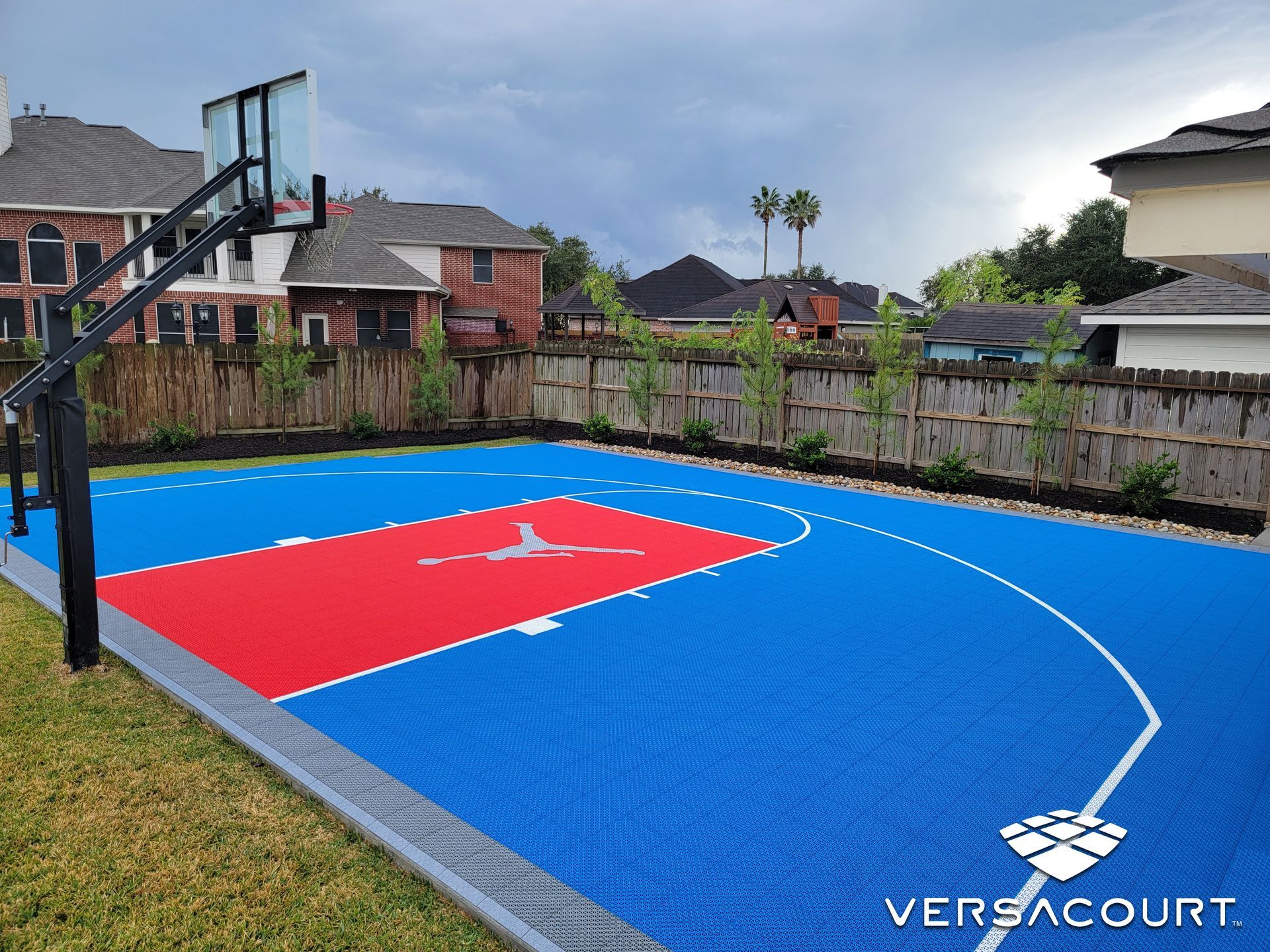 A blue and red basketball court with a basketball hoop in the backyard of a house.