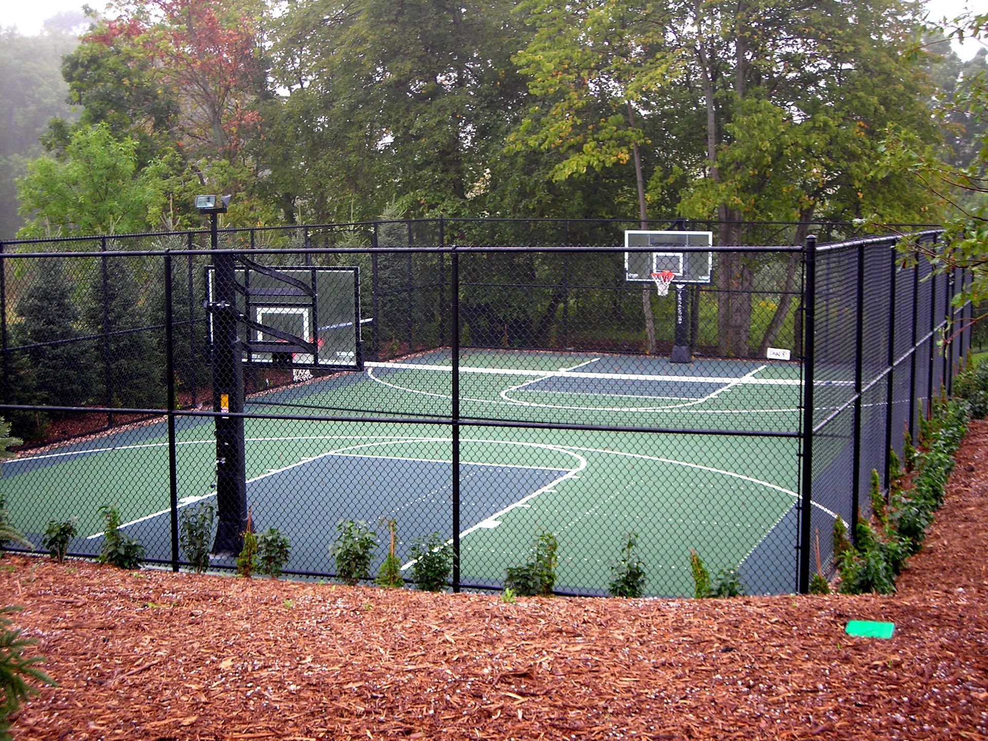 A basketball court behind a chain link fence with trees in the background