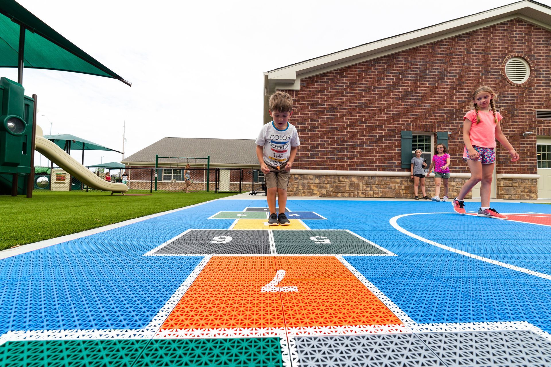 A boy and a girl are playing hopscotch in a playground.