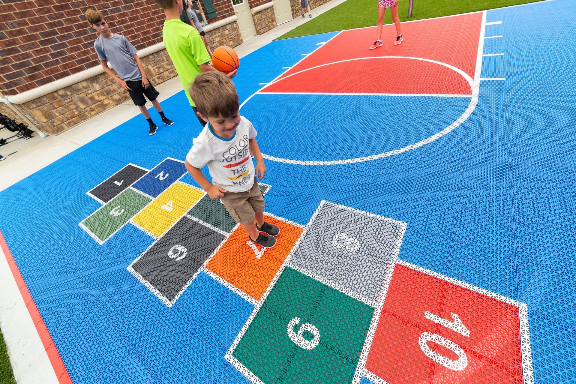 A young boy is playing hopscotch on a basketball court.