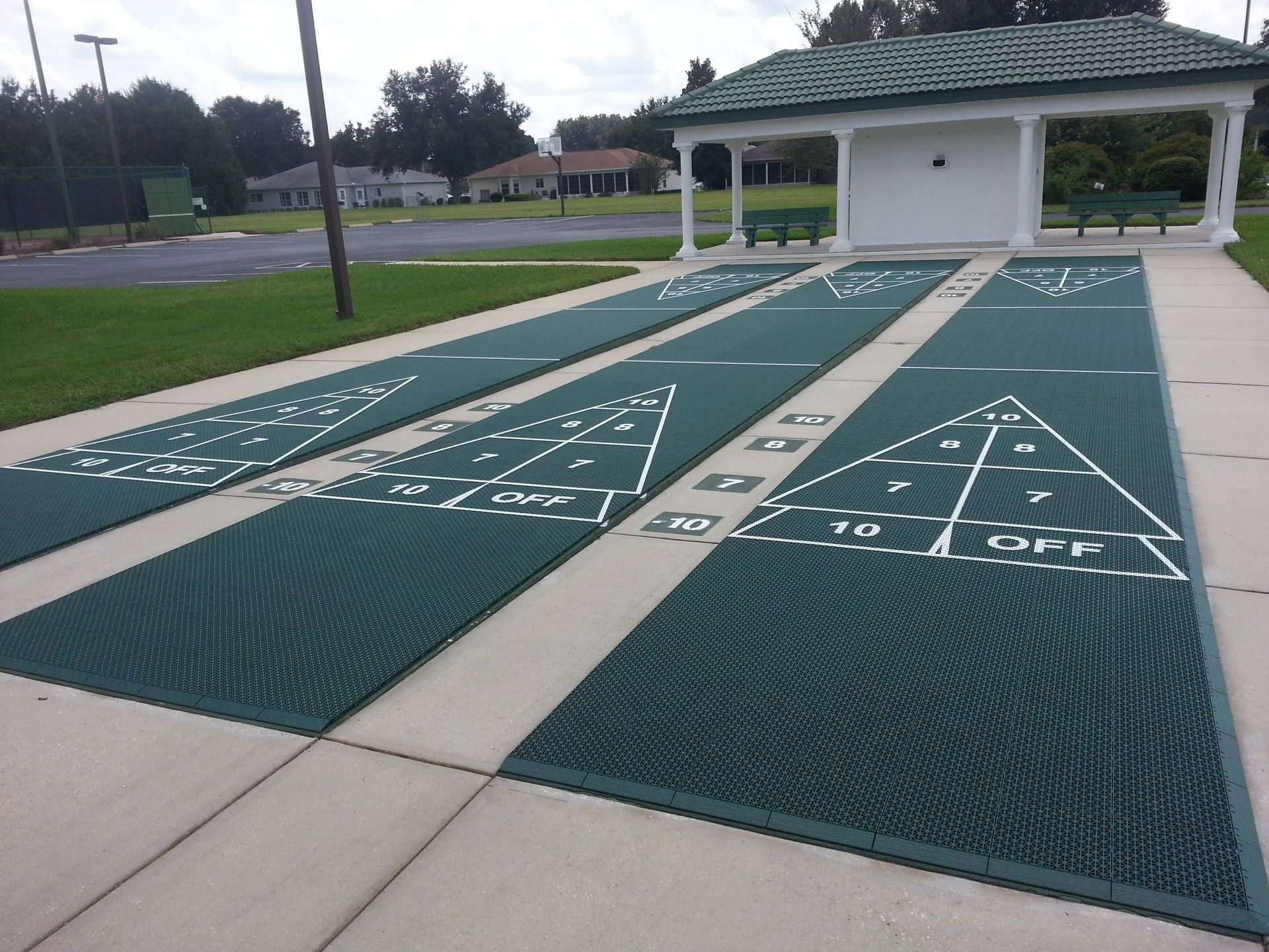 A shuffleboard court in a park with a white building in the background