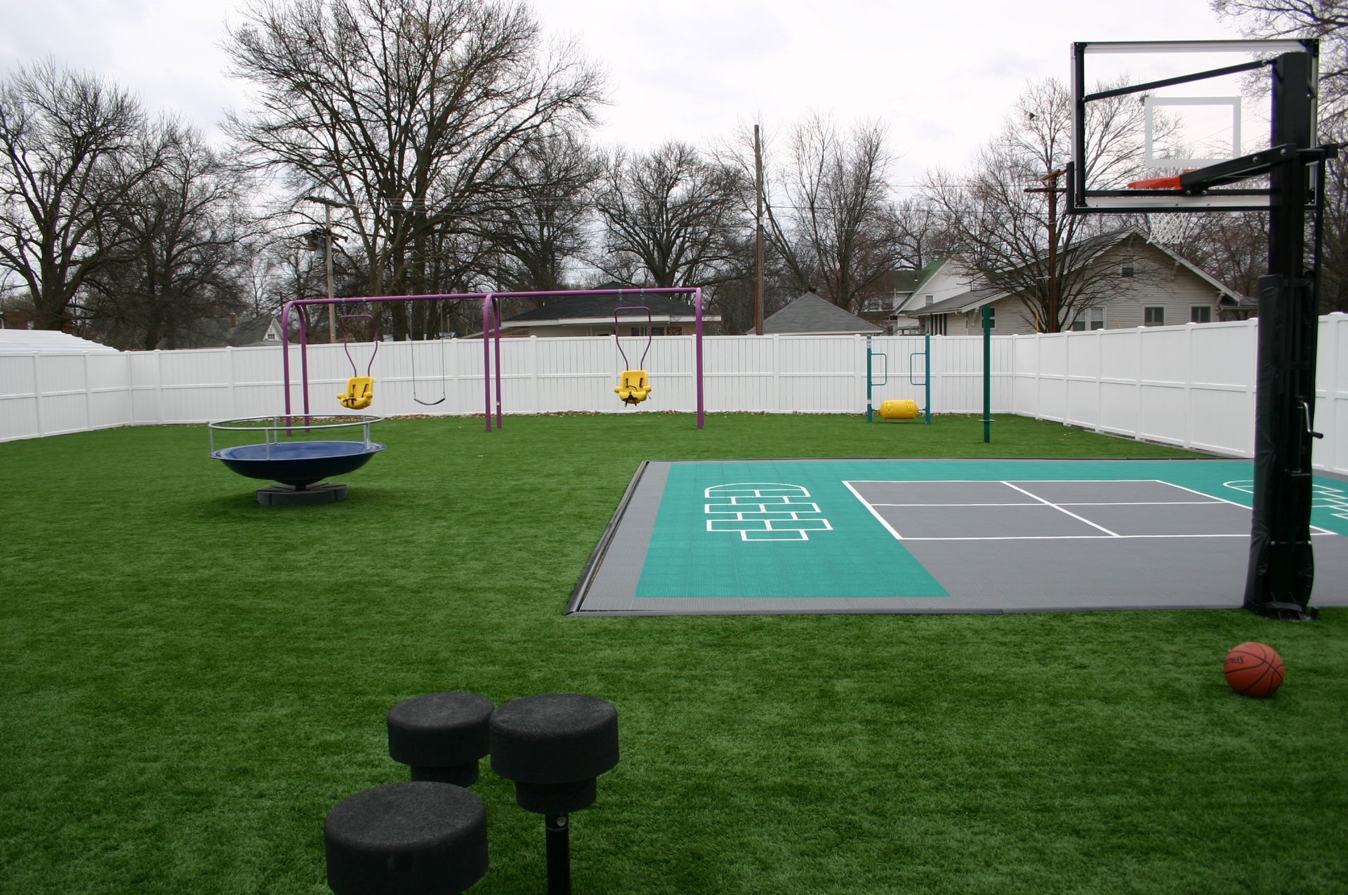 A backyard with a basketball court , swings , and a trampoline.