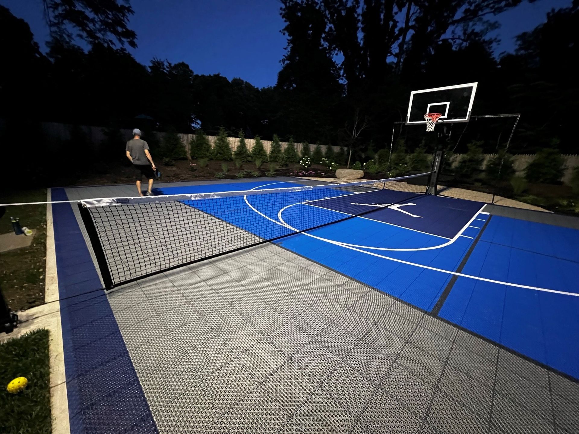 A man is playing tennis on a basketball court at night