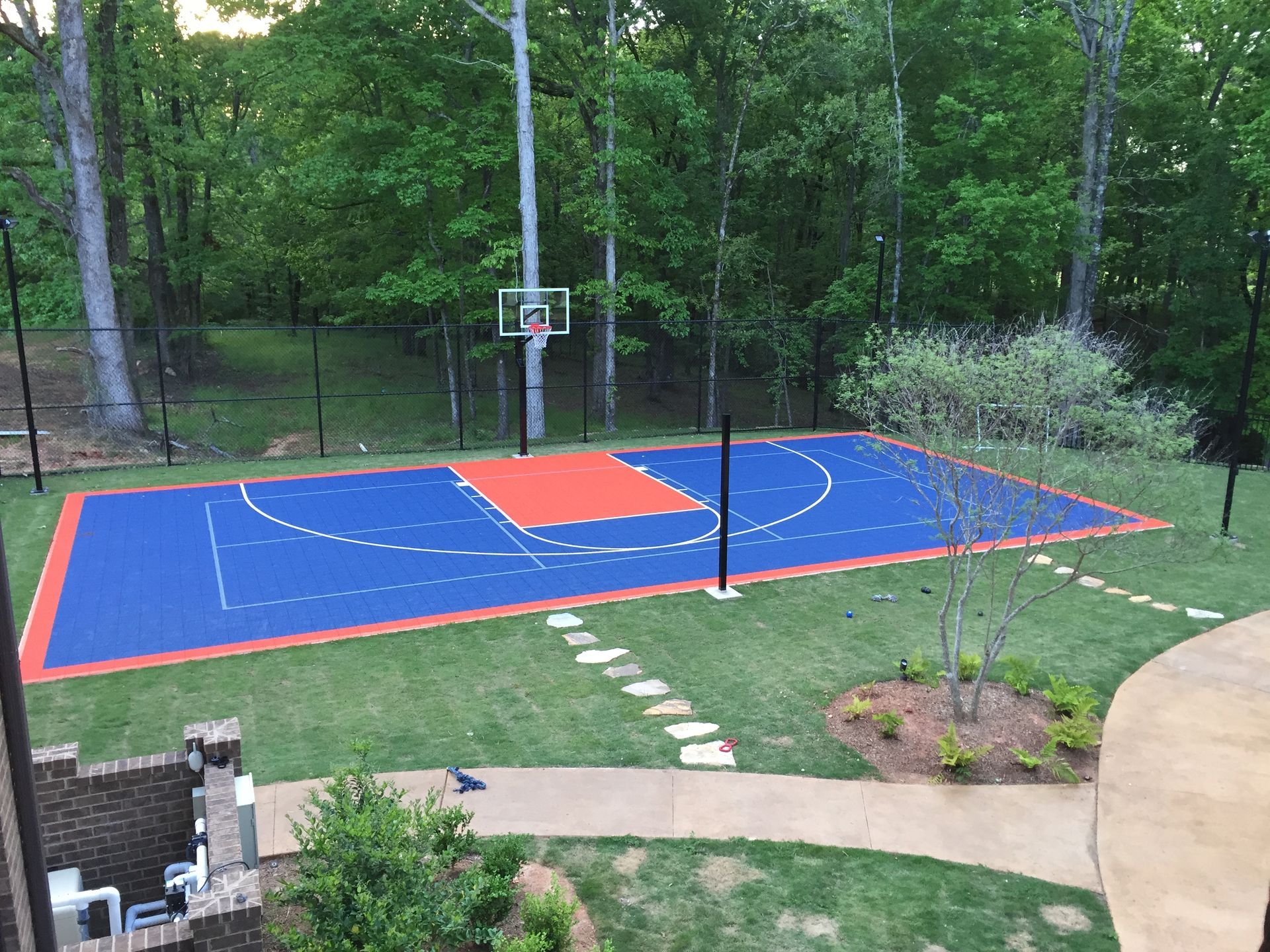 An aerial view of a basketball court in a backyard surrounded by trees.