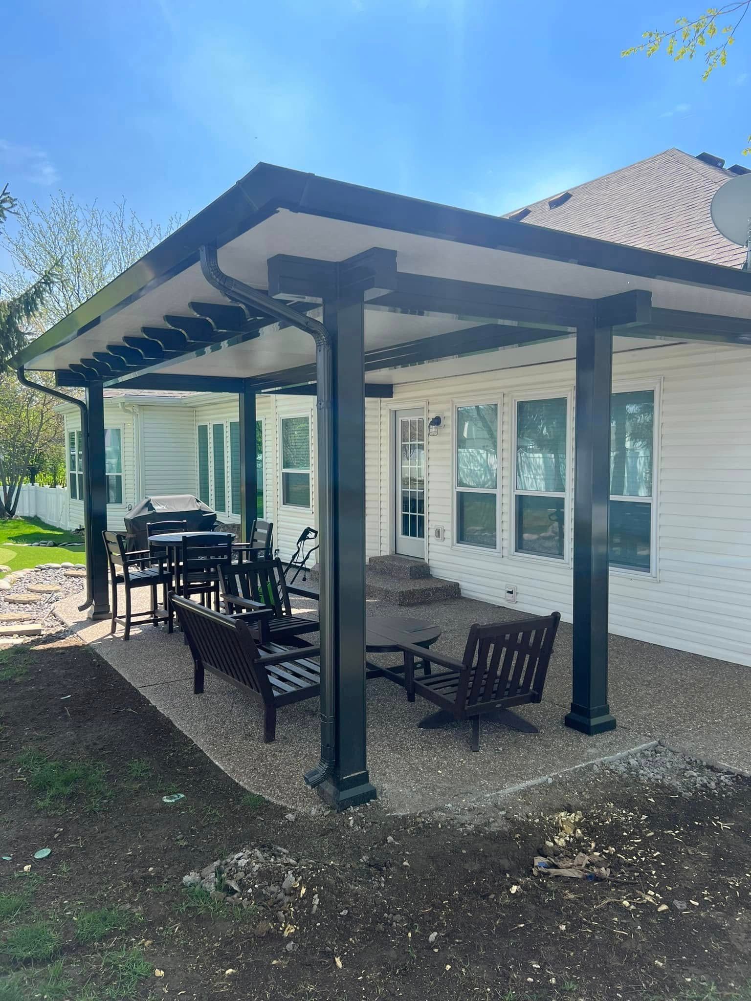 A white house with a covered patio with a table and chairs underneath it.