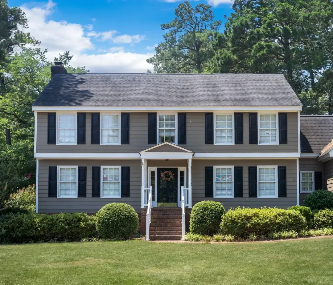 A large house with black shutters and a large lawn in front of it.