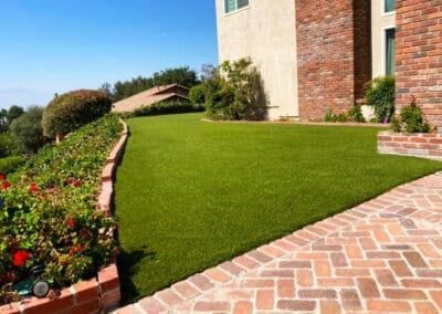 A brick walkway leading to a house with a lush green lawn.