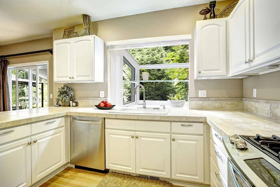 A kitchen with white cabinets , stainless steel appliances , and a large window.