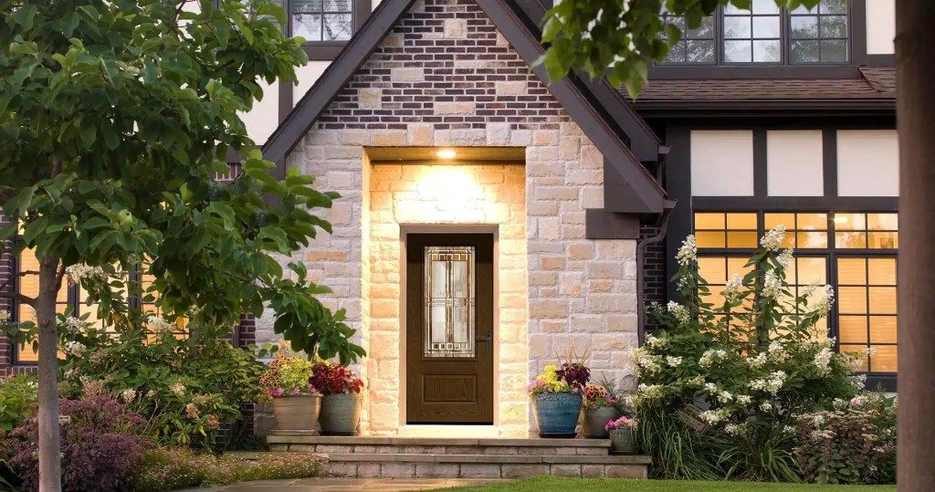 The front door of a brick house with a brown door is lit up at night.