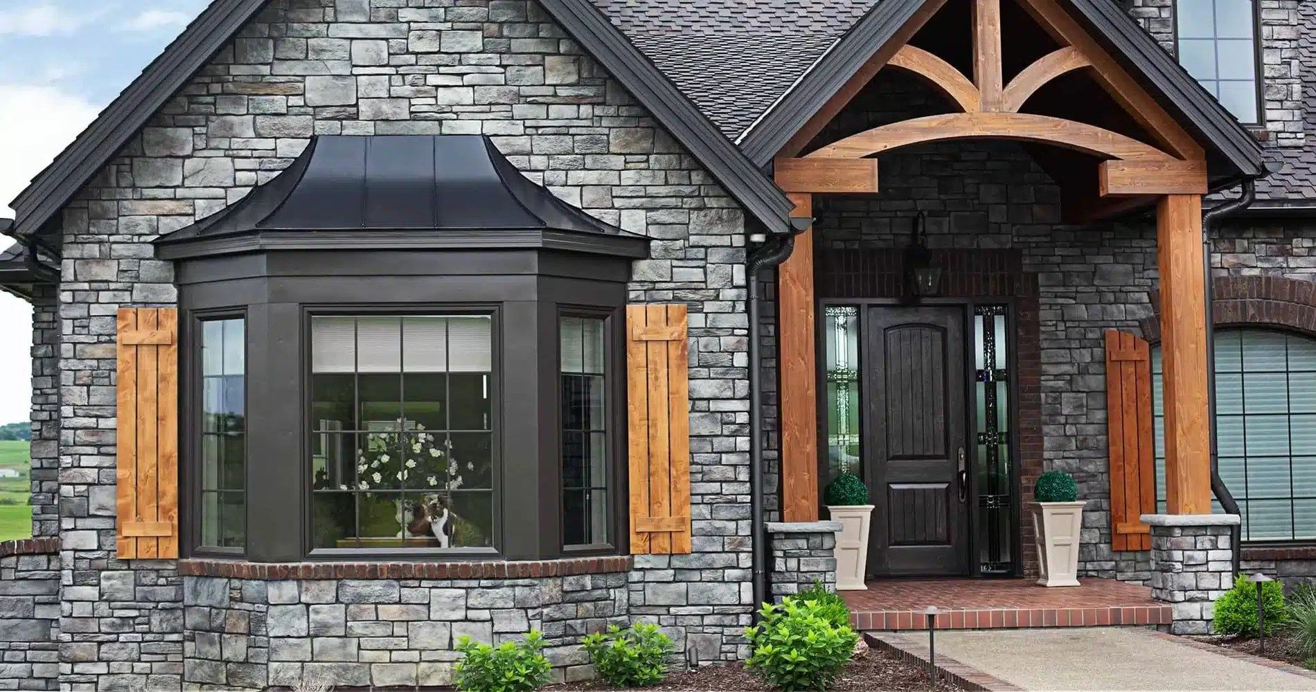 A large stone house with a large bay window and a wooden porch.