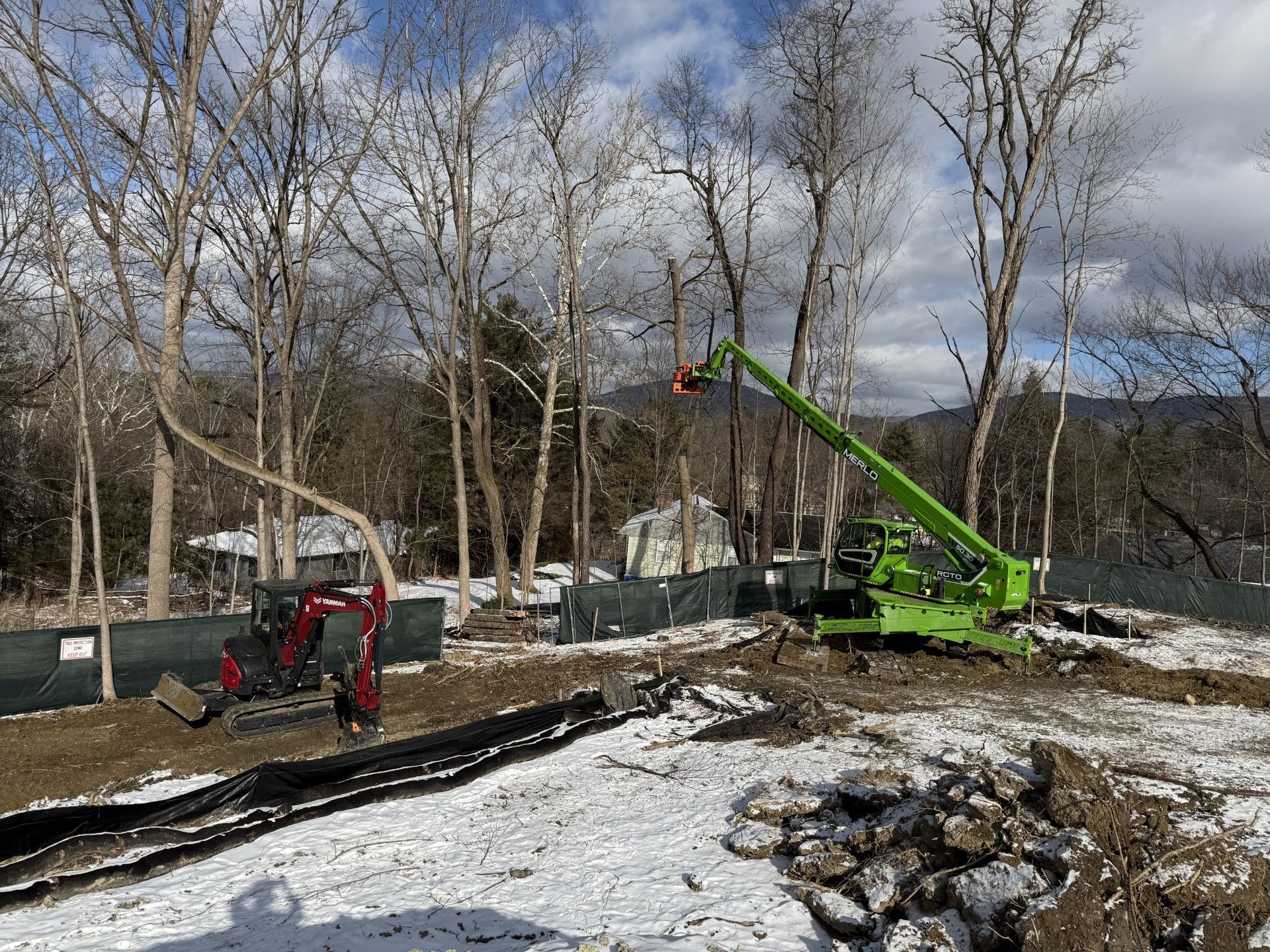 A construction site with a green crane and a red excavator in the snow.