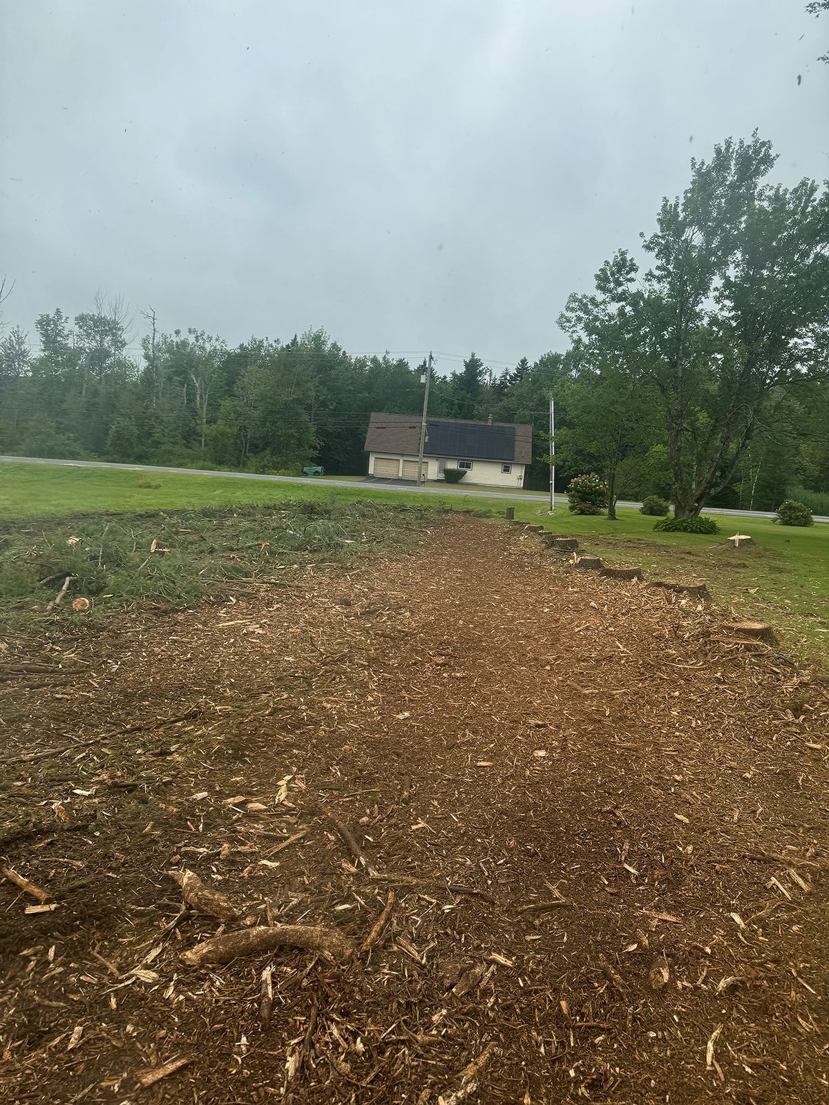 A pile of wood chips in a field with a house in the background