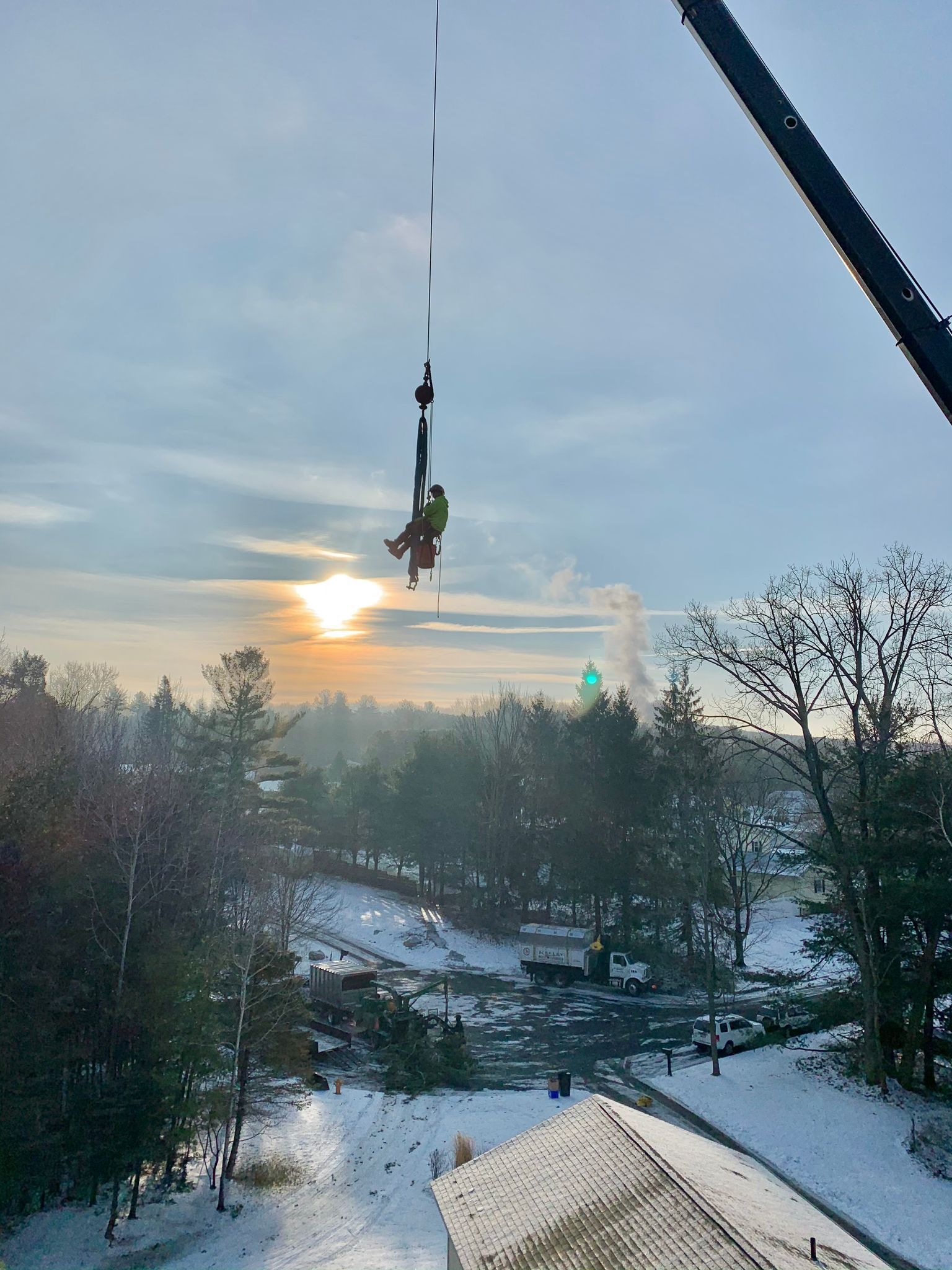 A person is hanging from a crane in the air over a snowy area.
