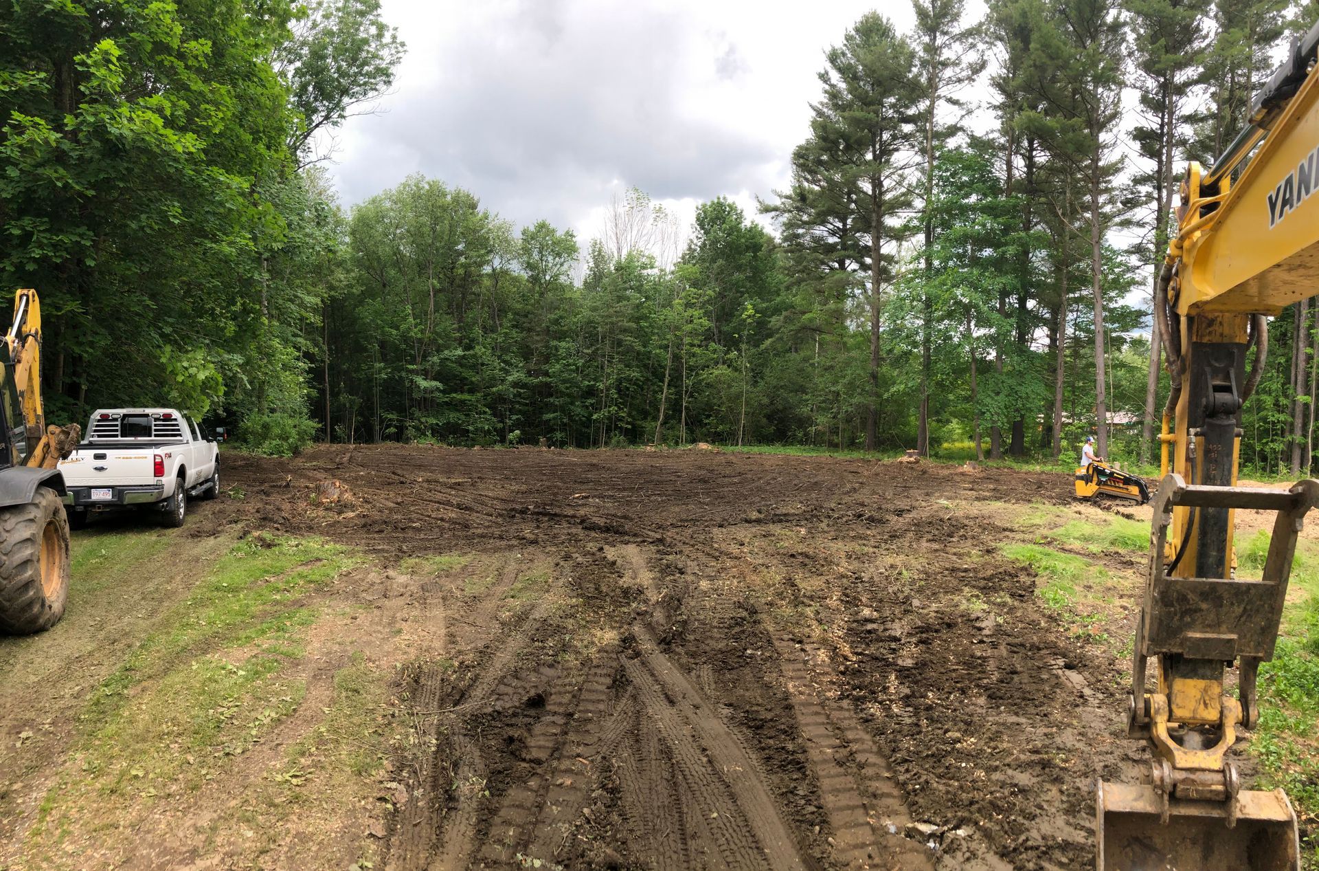 A white truck is parked in a dirt field next to a yellow excavator.