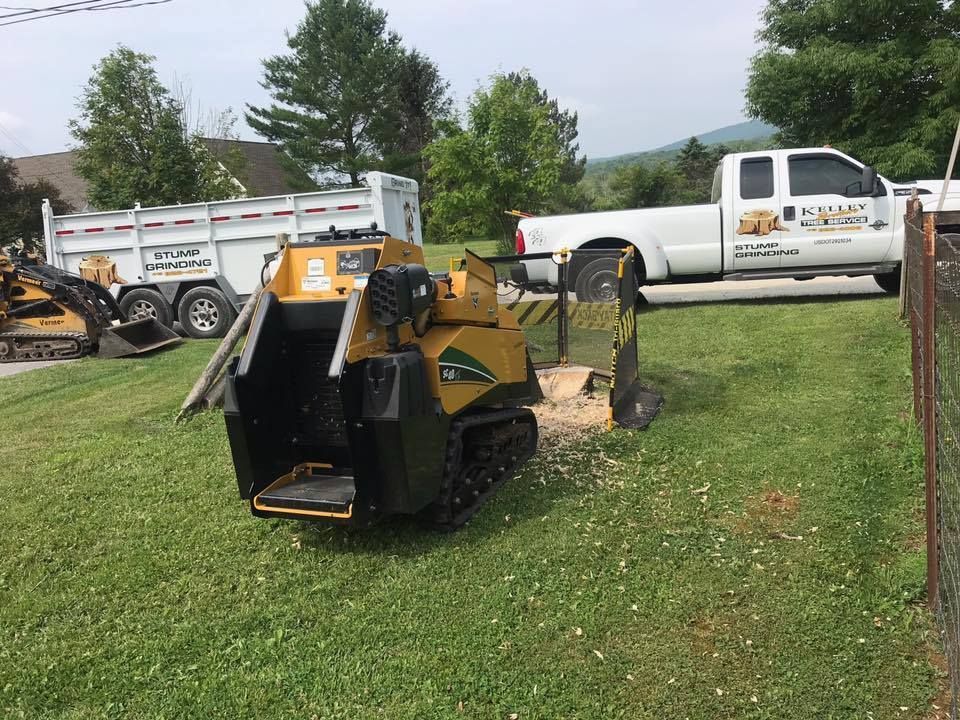 A stump grinder is sitting in the grass next to a truck.