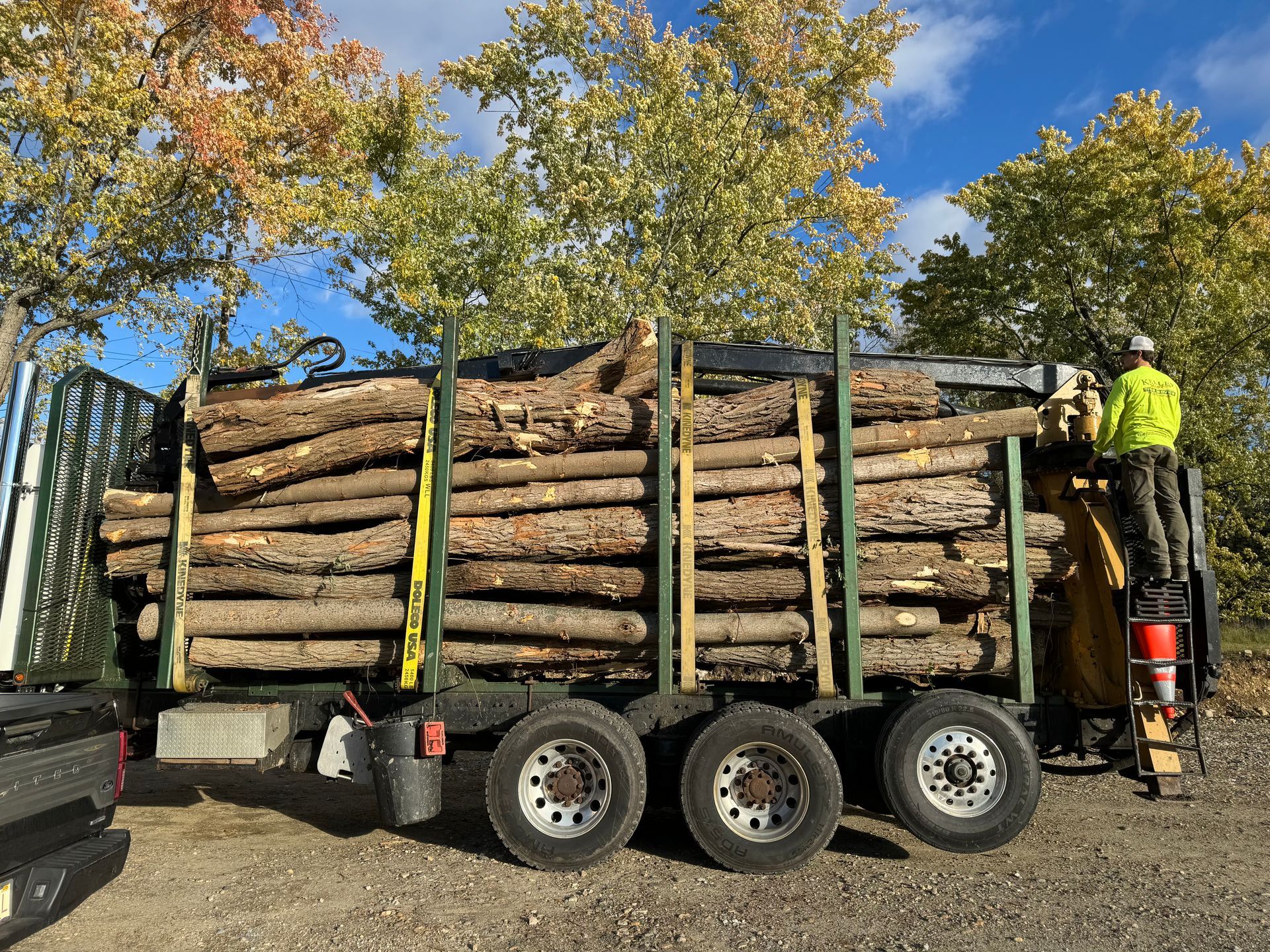 A truck filled with logs is parked in a gravel lot