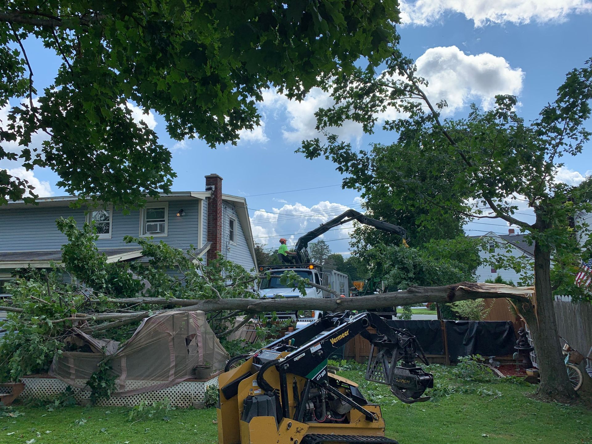 A tractor is cutting down a tree in front of a house.
