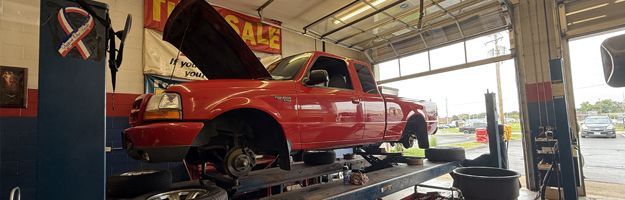 Red pickup truck on a lift inside an auto repair shop, hood open during service.