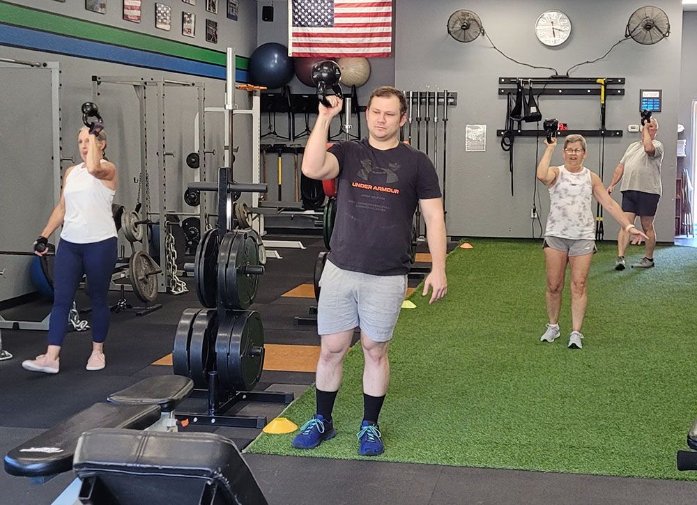A man is holding a kettlebell in a gym with other people.