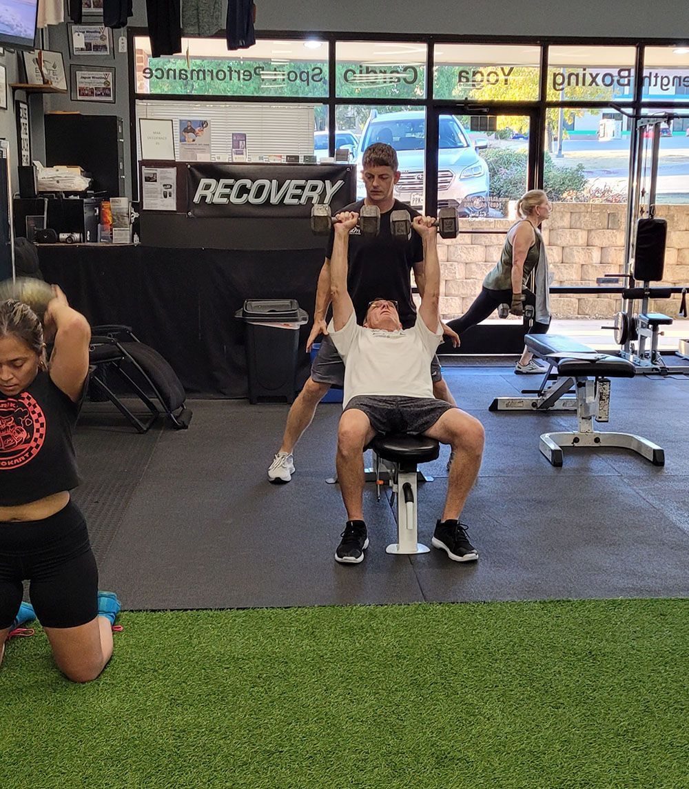 A man is sitting on a bench in a gym lifting dumbbells.