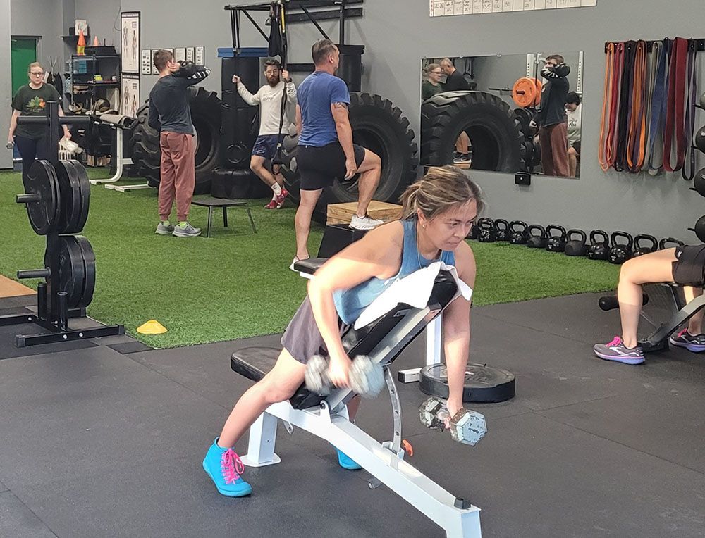 A woman is lifting a dumbbell on a bench in a gym.