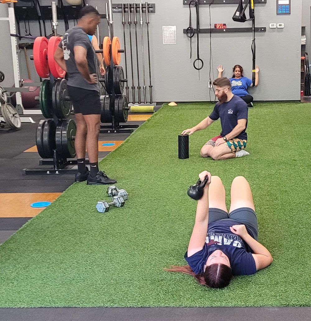 A woman is laying on the floor in a gym with a kettlebell.