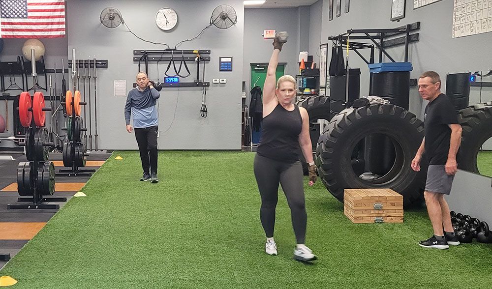A woman is lifting a dumbbell over her head in a gym.