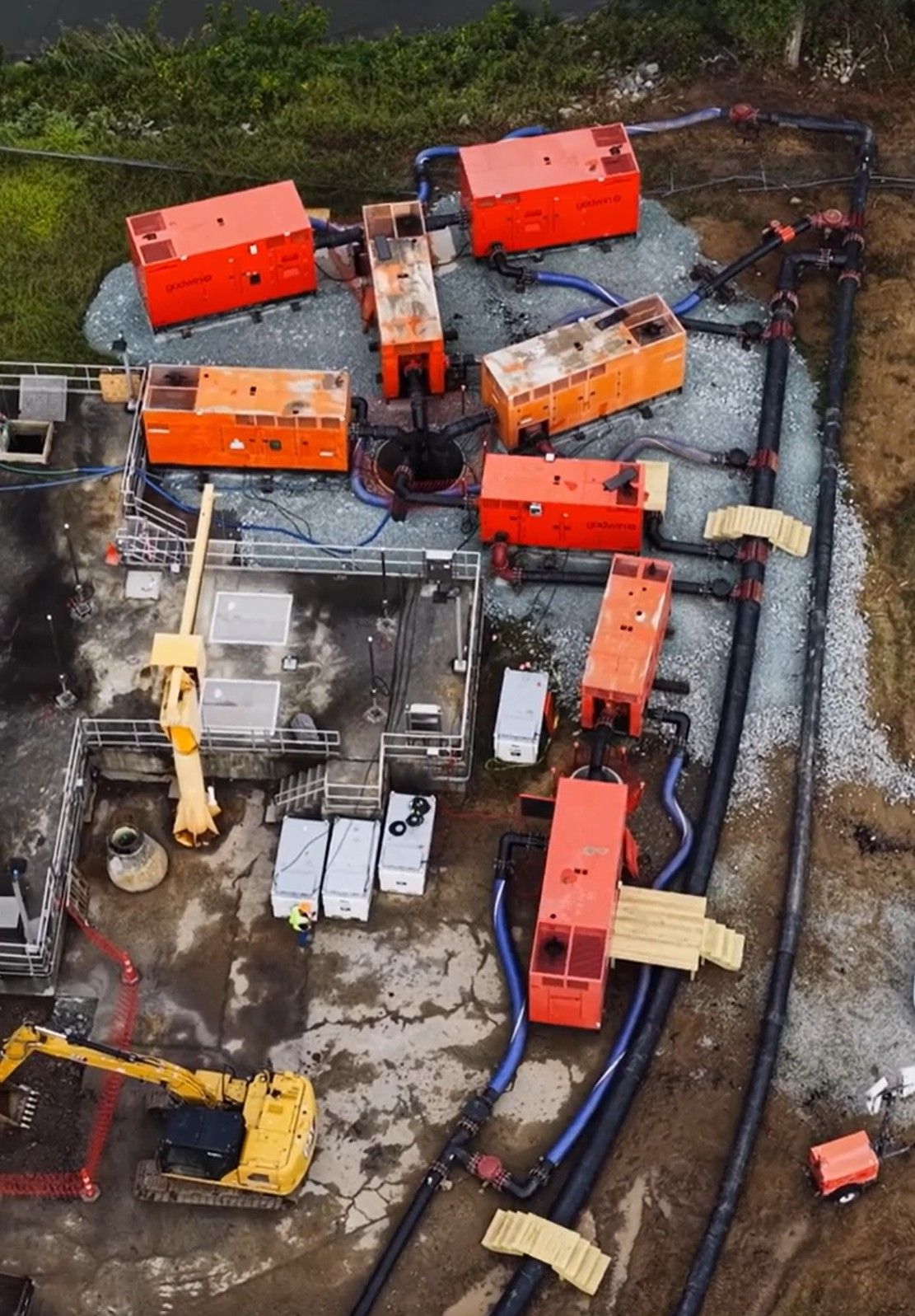 An aerial view of an industrial pump station featuring multiple orange pump units, piping, and construction equipment.