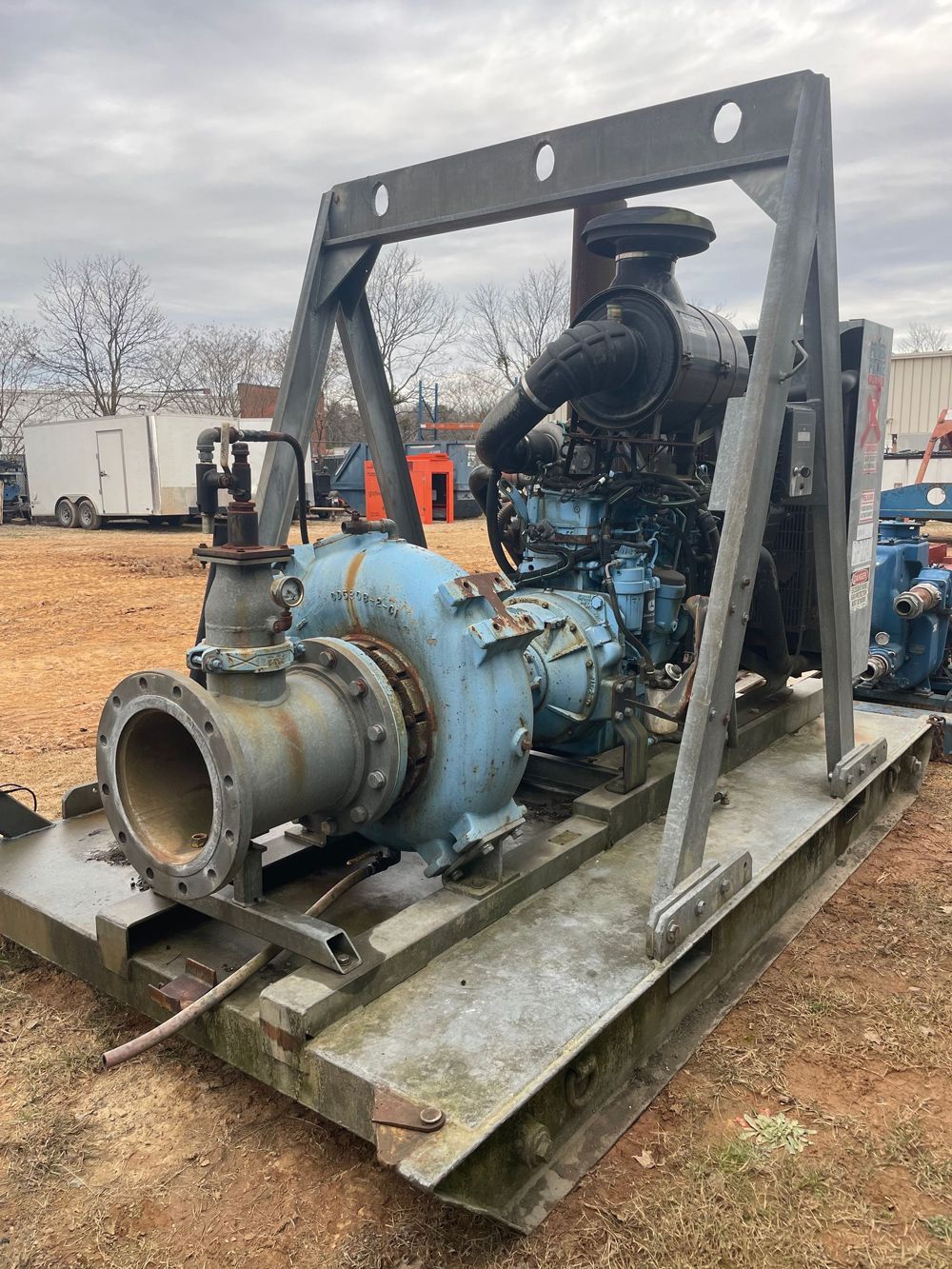 Blue industrial water pump on a metal base with a diesel engine, sitting outdoors on brown dirt.
