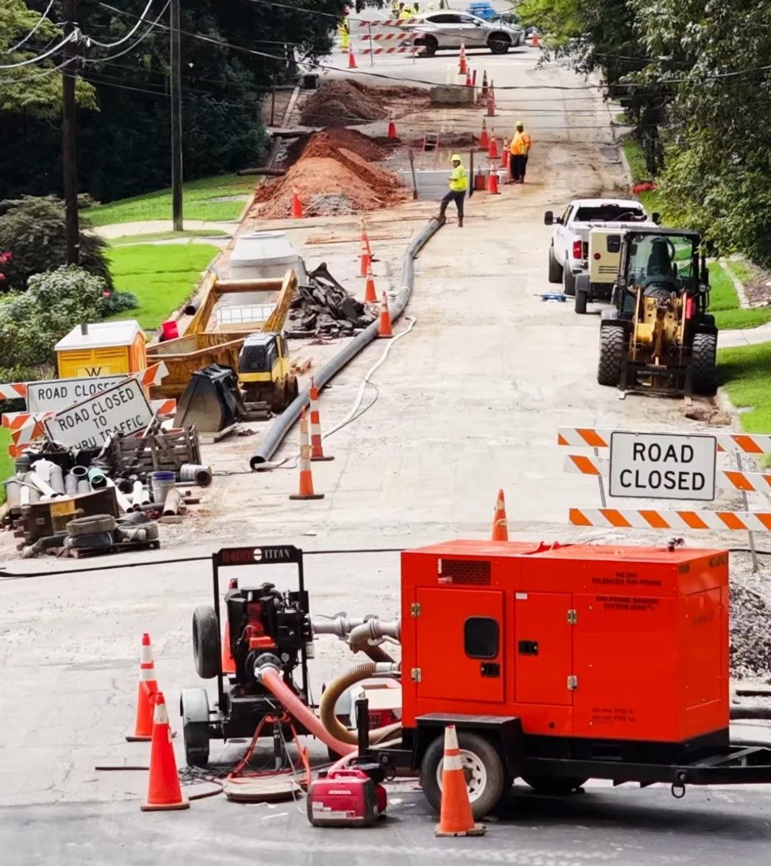 Road construction site. Closed road with machinery, orange cones, and workers.
